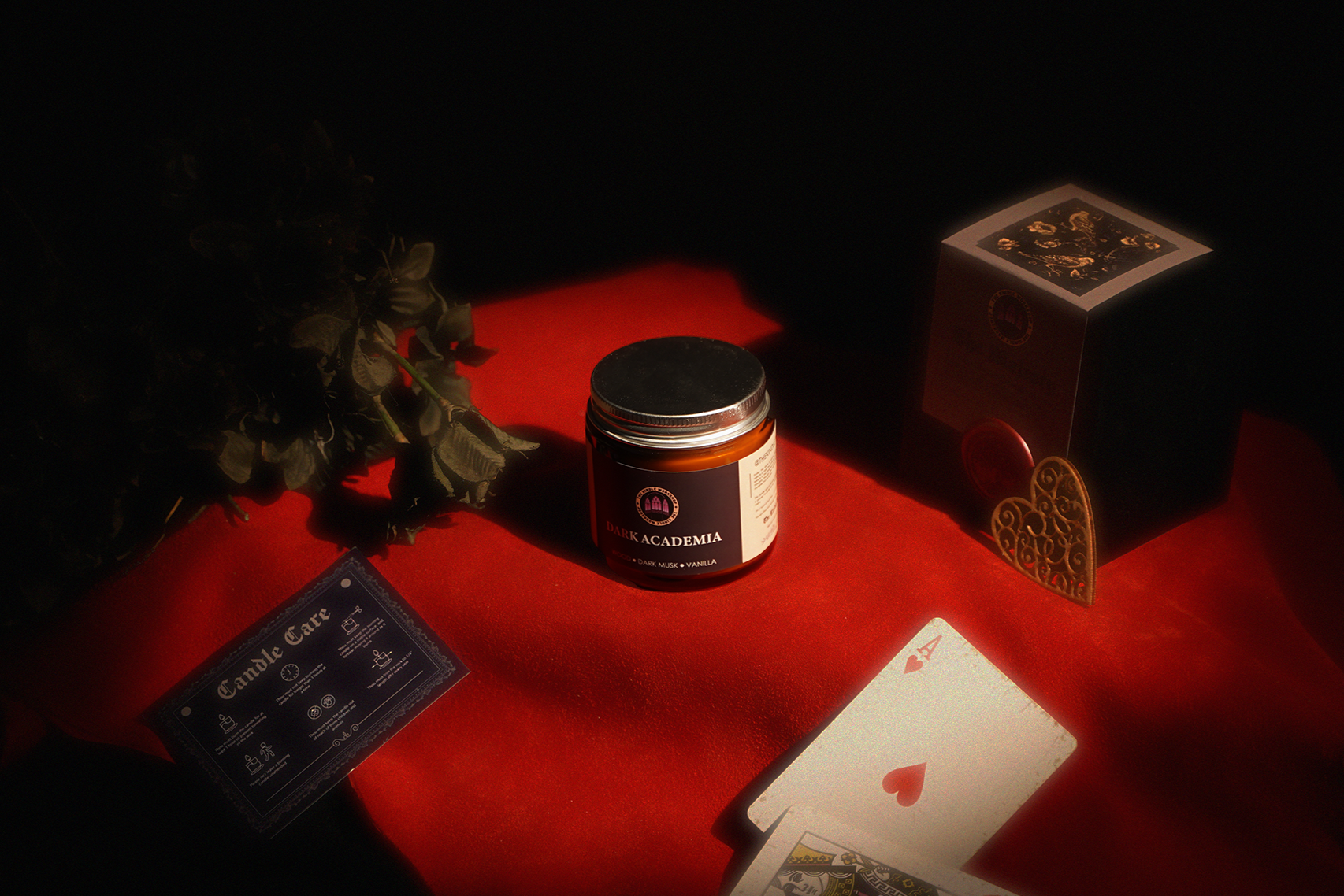 Candle, playing cards, and a box on a red surface with a dark background